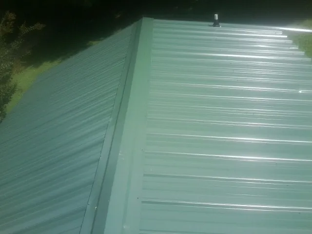 New green metal panels meeting at the ridge of a roof — Flat Roof Repair work by our crew in East Rochester