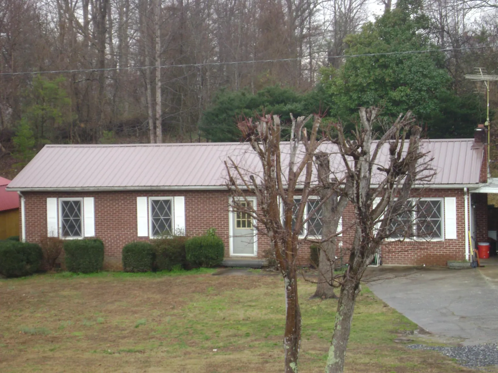 Mauve metal roof on a brick ranch home behind bare trees in East Rochester
