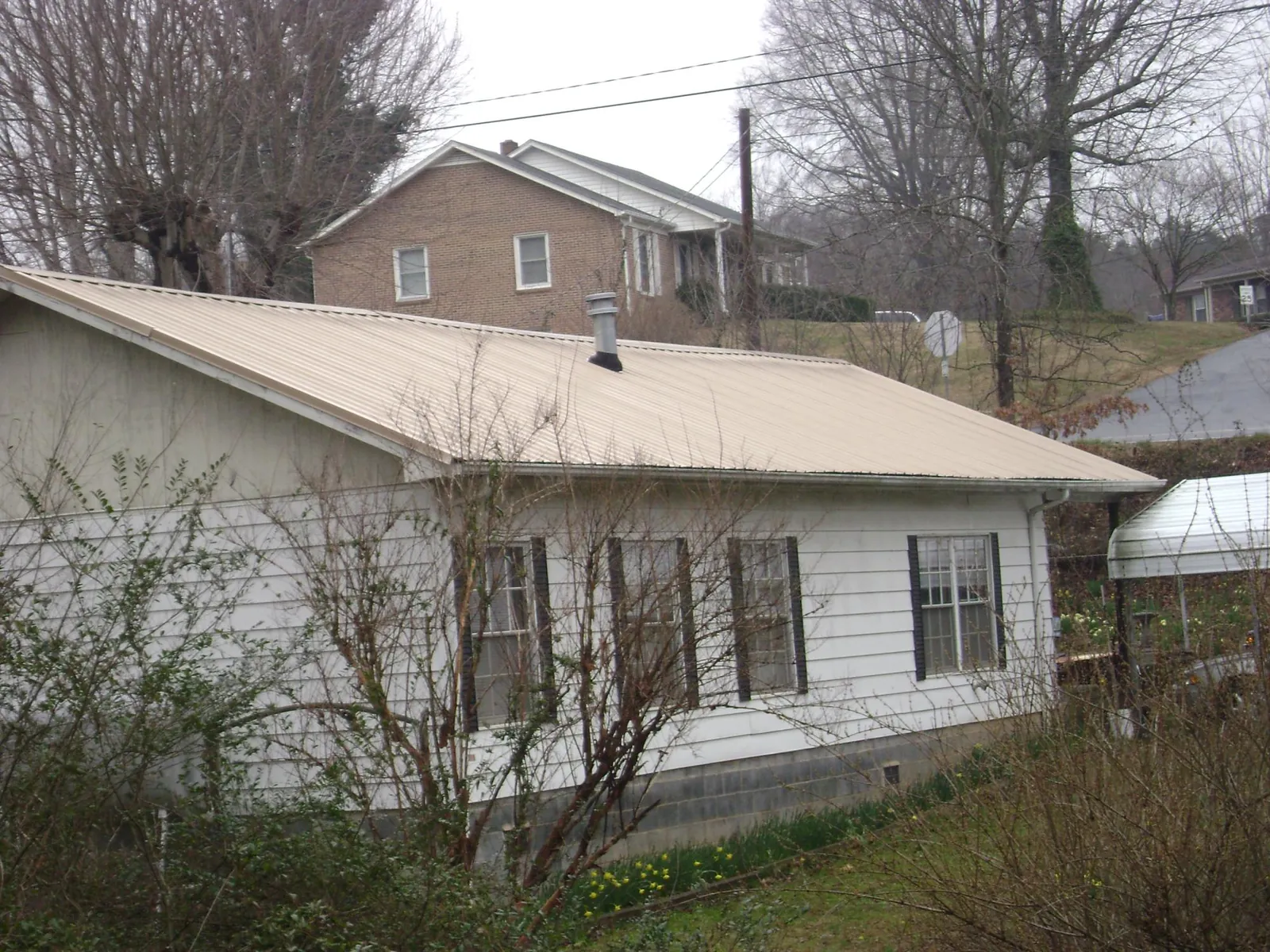 Tan metal roof on a white sided house set into a hillside — Commercial Roofing by Roofing Brothers in East Rochester