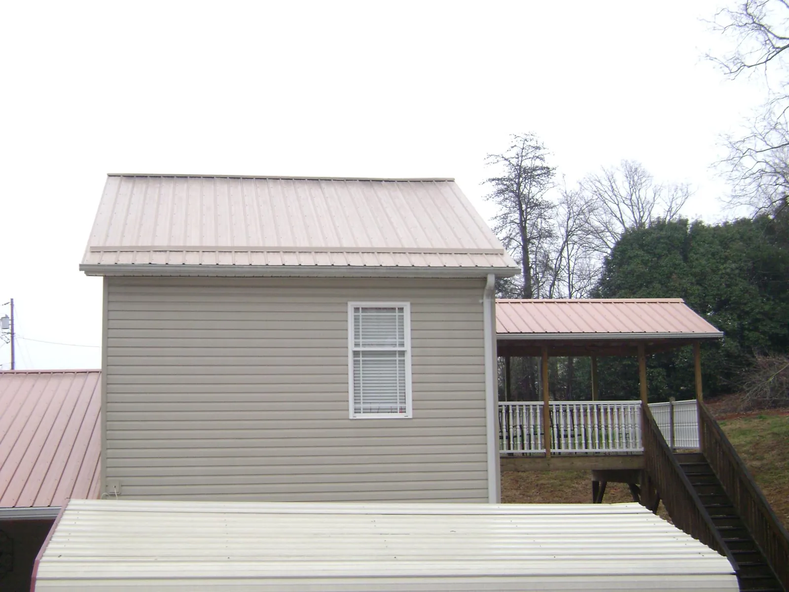 Tan metal roofs on a two story addition and attached porch, from a Roof Replacement job in East Rochester